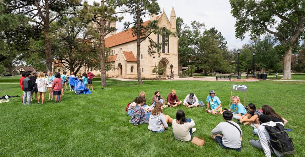 Students gathering on a green quad with Shovel Chapel in the background.